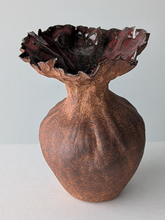 Bronze vase with textured surface and wavy rim on a white background
