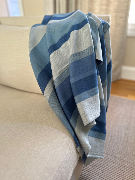 Blue and gray striped blanket draped over a chair in a room with a window and carpet.