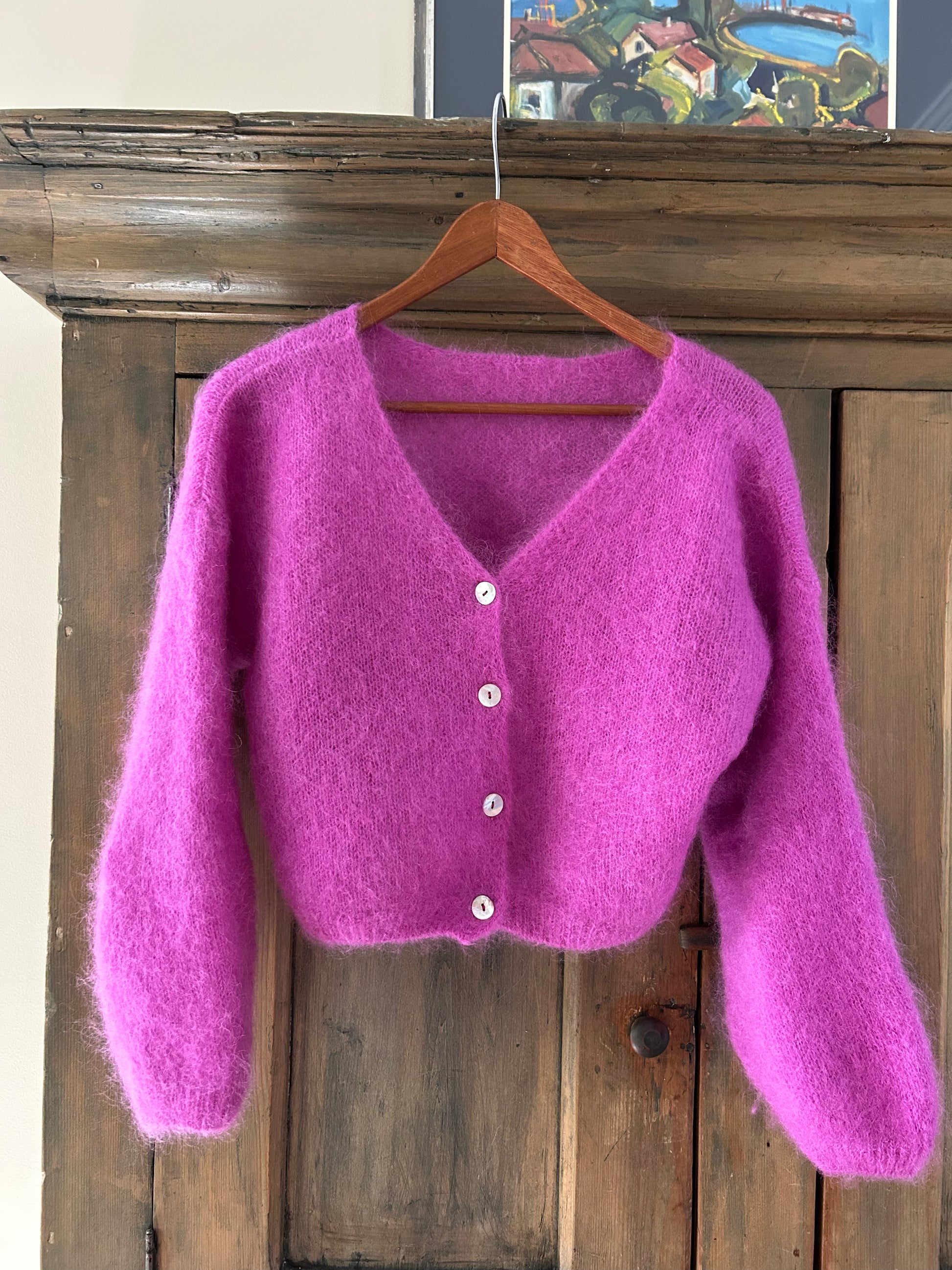 Purple mohair cardigan on a wooden hanger against a wooden background