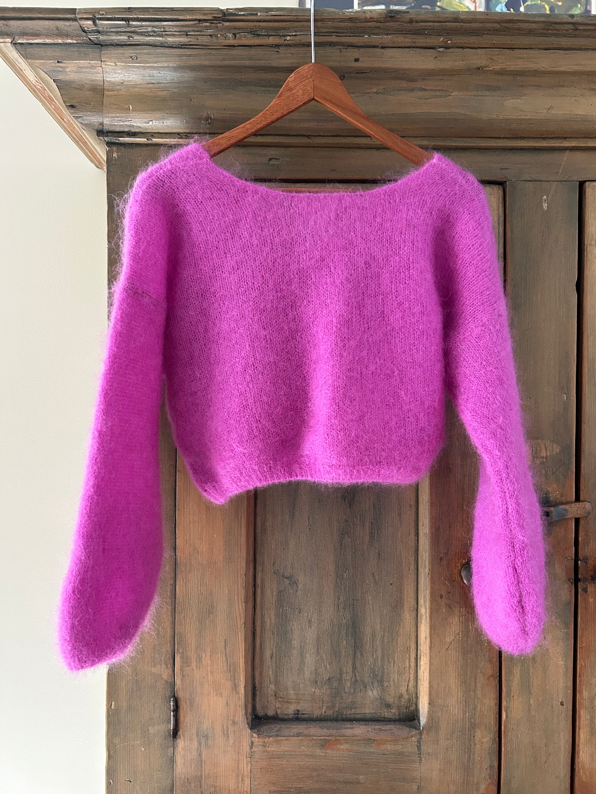 Purple sweater on a wooden hanger against a wooden door background