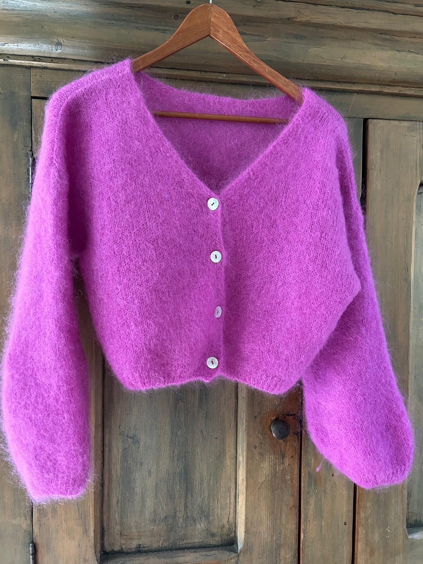 Purple cardigan on a wooden hanger against a wooden background