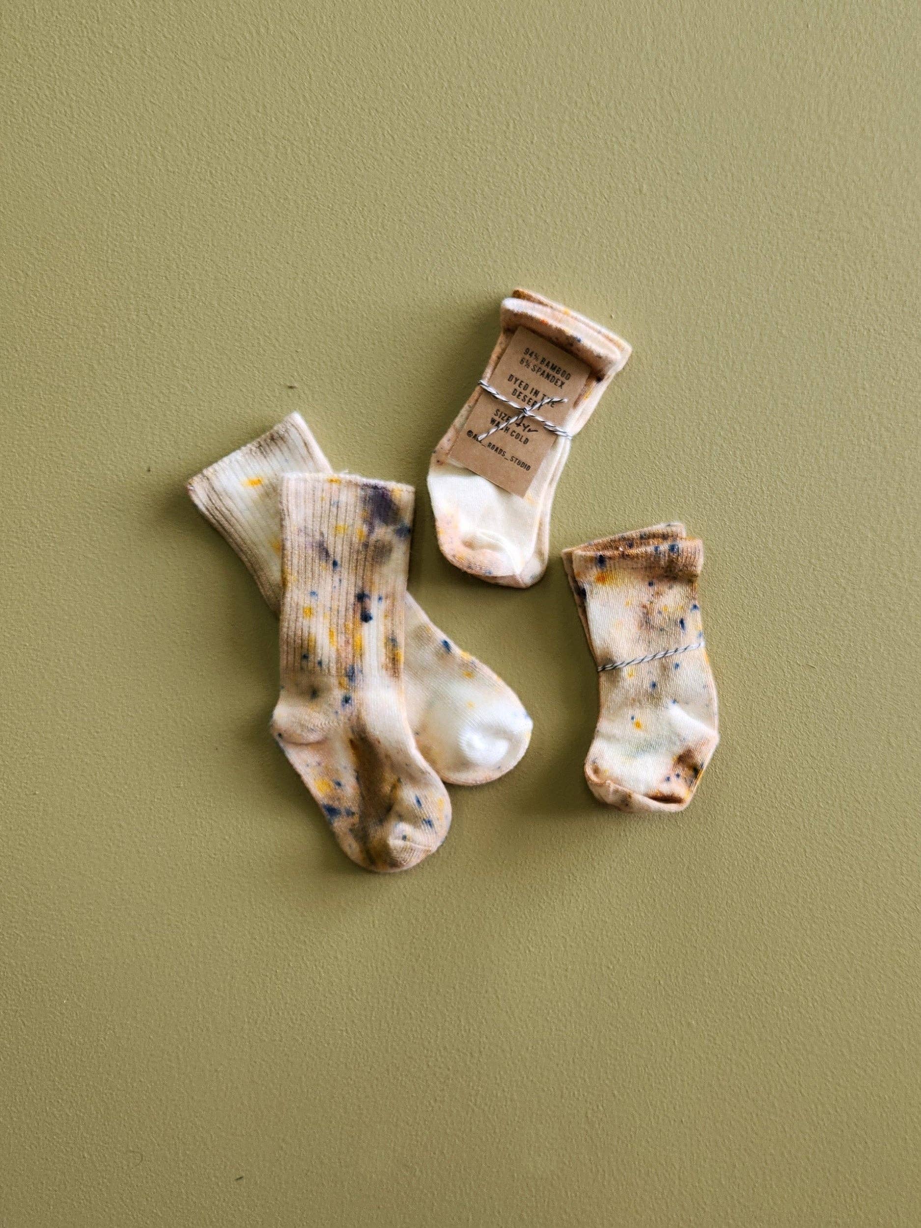 Three pairs of baby socks with natural patterns on a green background
