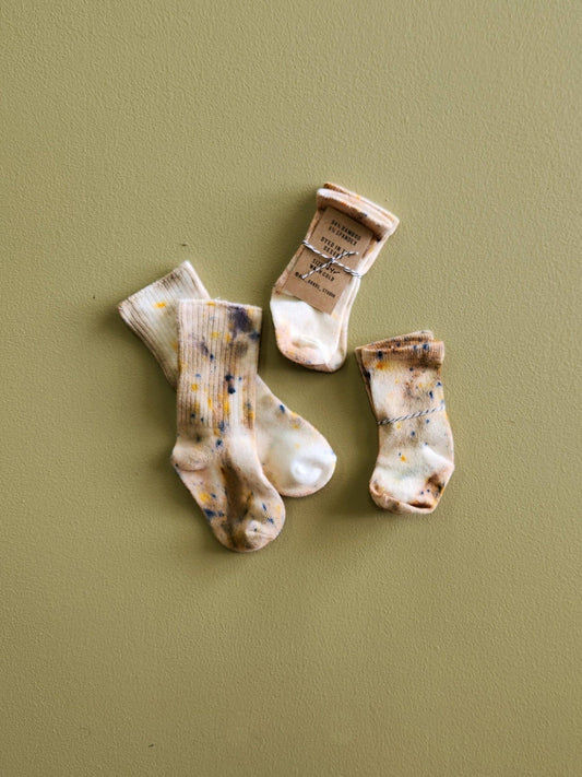 Three pairs of baby socks with natural patterns on a green background
