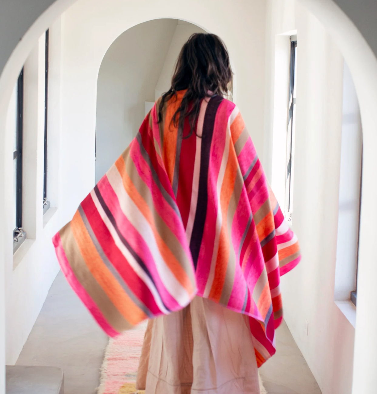 Person wearing a colorful striped shawl in a minimalistic room.
